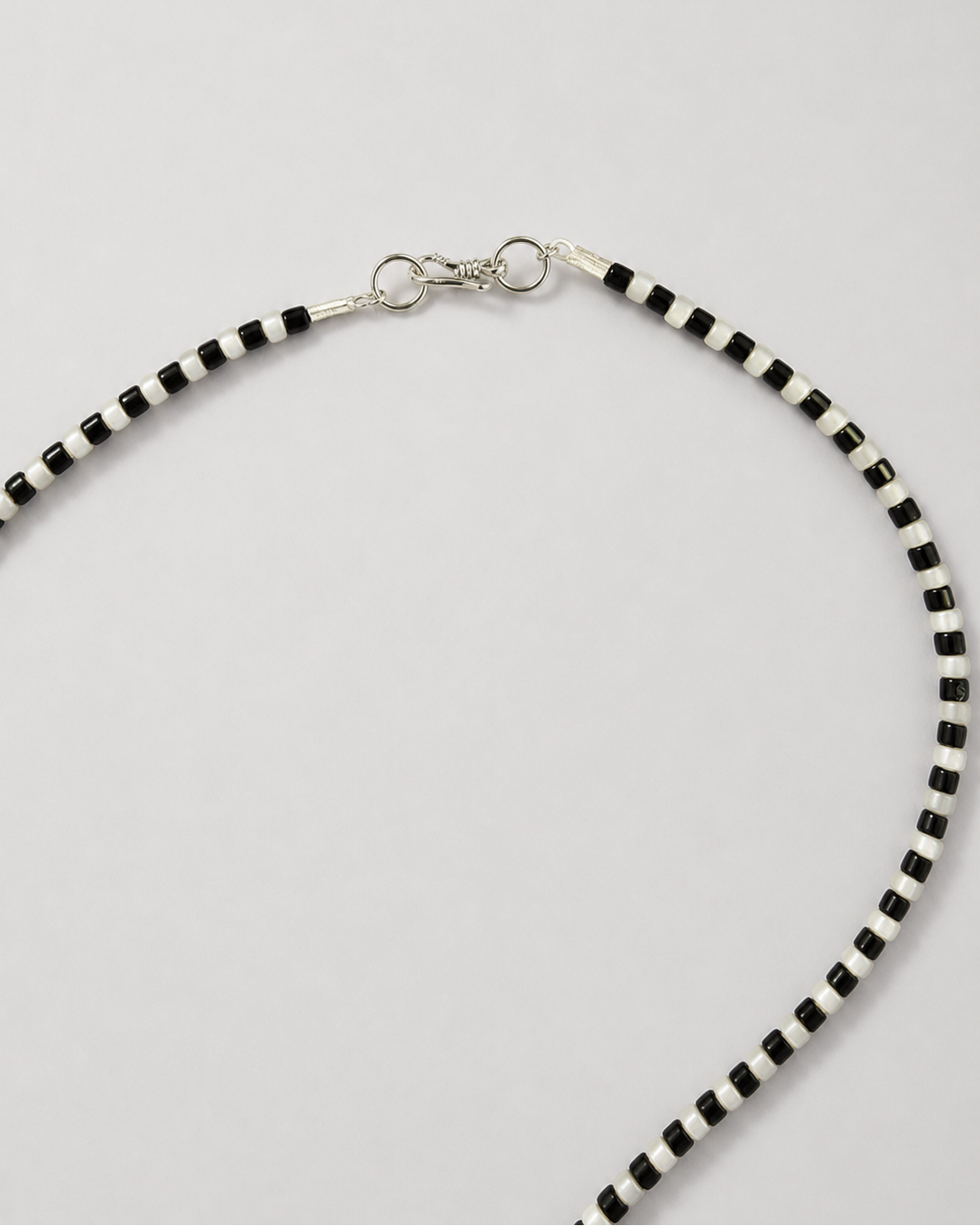 A beaded necklace with alternating black and white cylindrical beads, featuring a silver-toned lobster clasp closure, shown on a light gray background.