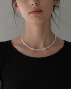 A woman wearing a delicate silver beaded necklace with a black top, photographed against a neutral gray background.