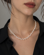 A close-up portrait of a woman wearing a delicate silver-toned necklace with small star-shaped charms, paired with a black collared shirt against a soft gray background.