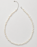 A delicate necklace made of small irregular white pearls on a silver-tone chain with an extender clasp, photographed on a light gray background.