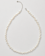 A delicate necklace made of small irregular white pearls on a silver-tone chain with an extender clasp, photographed on a light gray background.