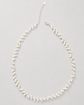 A delicate pearl necklace with a silver-tone chain extender and lobster clasp, displayed on a neutral light gray background.