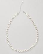 A delicate pearl necklace with a silver-tone chain extender and lobster clasp, displayed on a neutral light gray background.