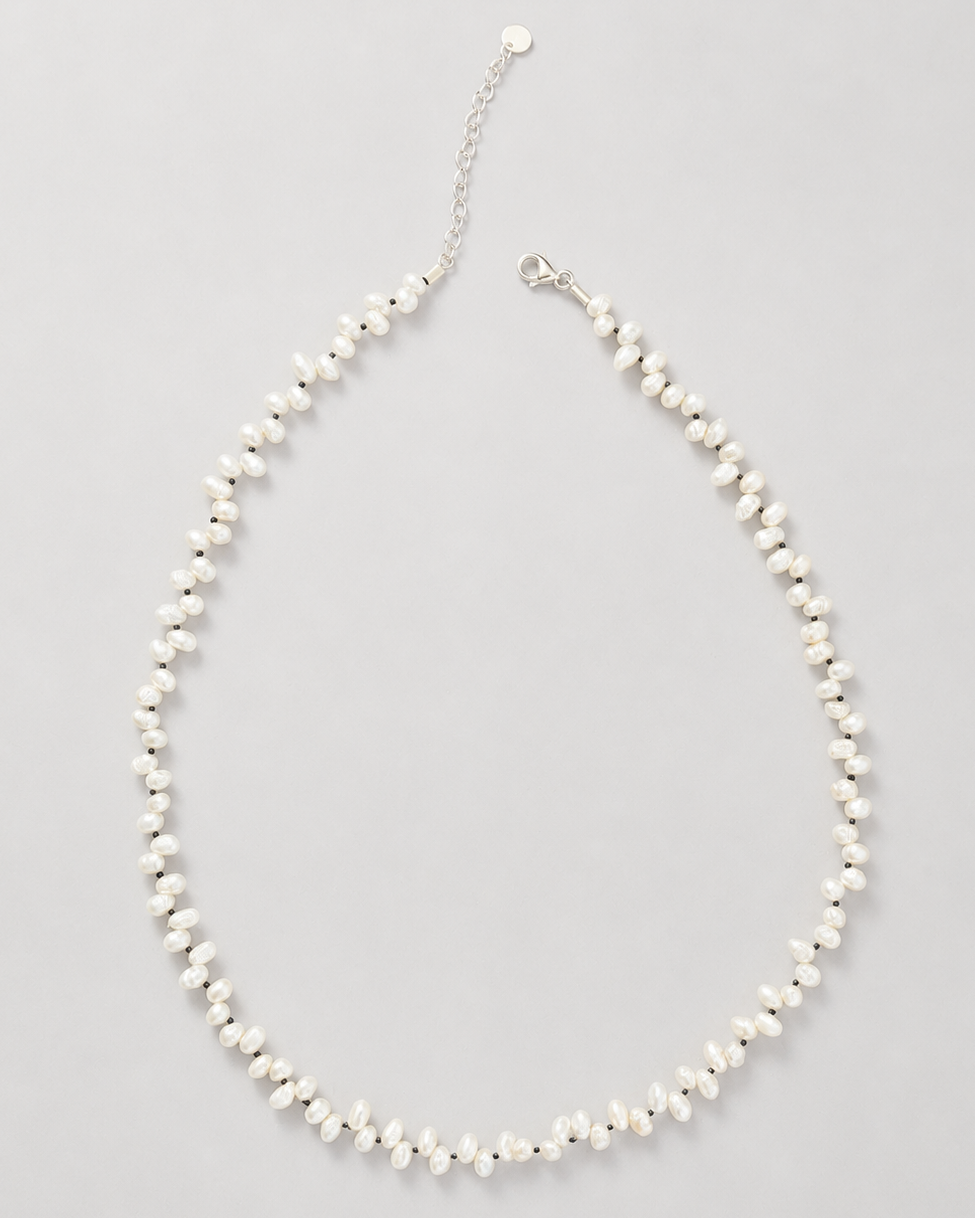 A delicate pearl necklace with a silver-tone chain extender and lobster clasp, displayed on a neutral light gray background.