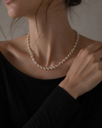 A close-up of a woman wearing a delicate strand pearl necklace with a black top, showing the necklace against her neck.