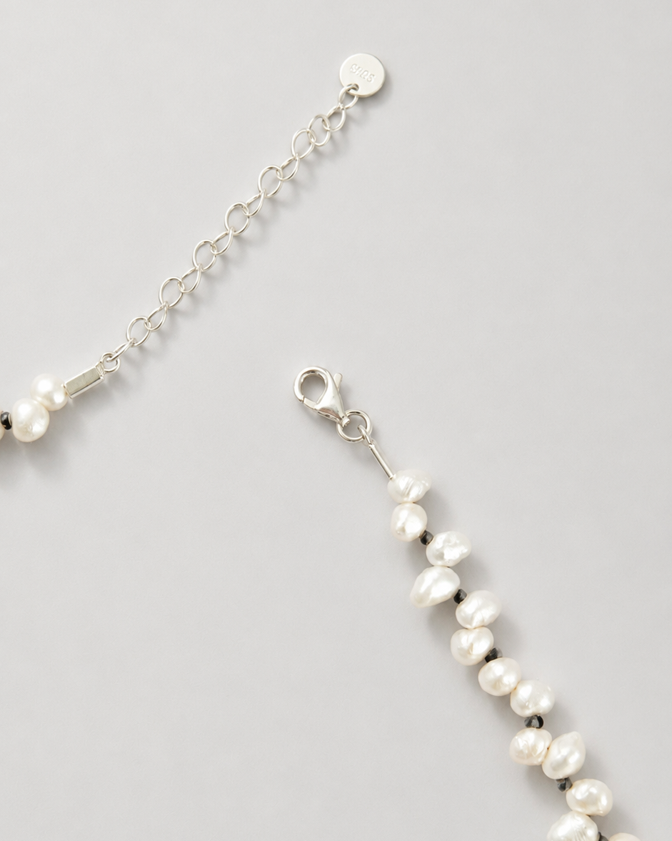 A close-up of a silver chain bracelet with irregular white freshwater pearls, showing the lobster clasp and extension chain on a light gray background.